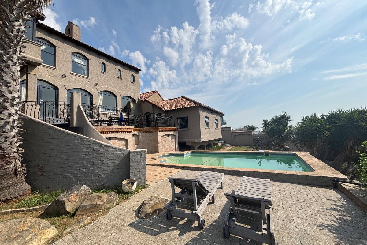 Rear exterior view featuring a swimming pool, paved patio area, and multi-story brick residence with arched windows and a balcony.