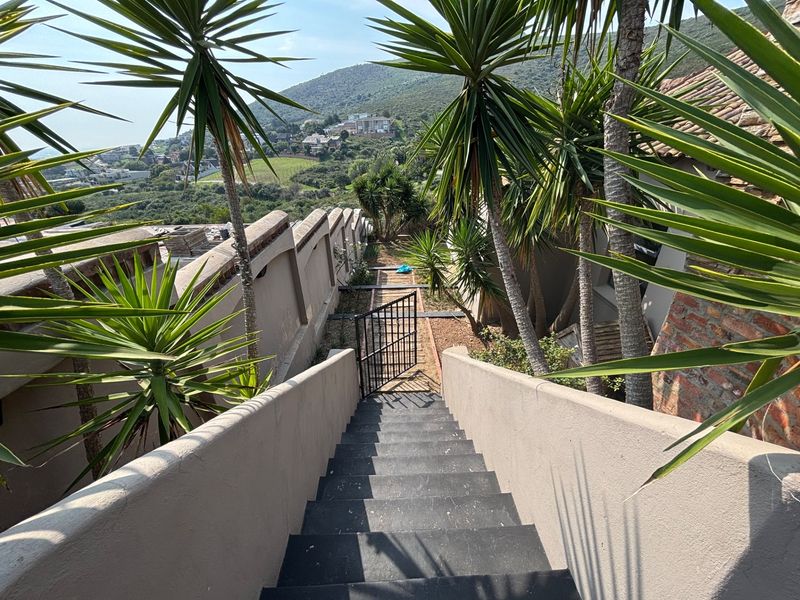 An outdoor staircase leading down to a lower garden area, featuring solid boundary walls and a metal gate with scenic hillside views.