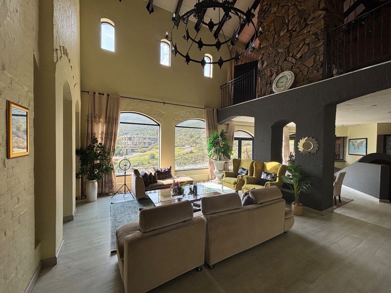 Spacious double-volume living room featuring a striking stone fireplace, arched windows with scenic views, and a mezzanine level overlooking the main area.