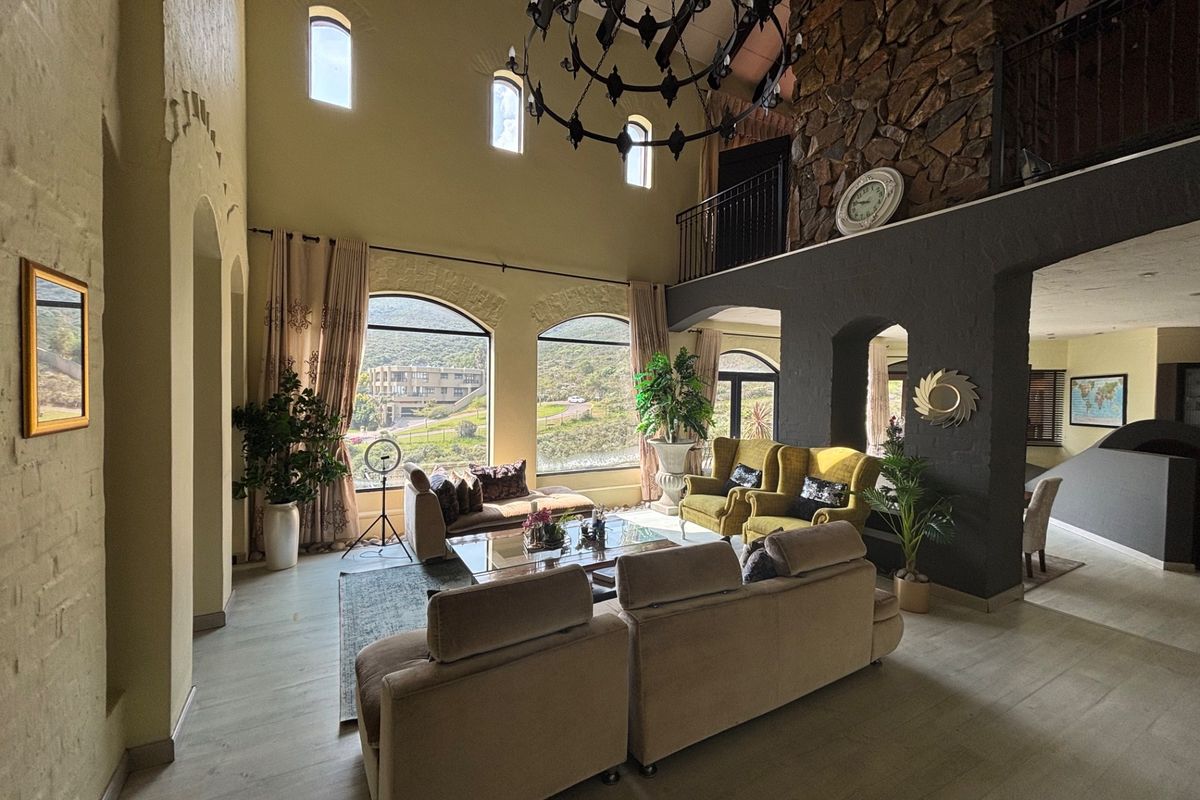 Spacious double-volume living room featuring a striking stone fireplace, arched windows with scenic views, and a mezzanine level overlooking the main area.