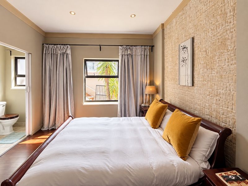Spacious bedroom featuring a textured stone accent wall, warm laminate flooring, recessed lighting, and direct access to an en-suite bathroom.