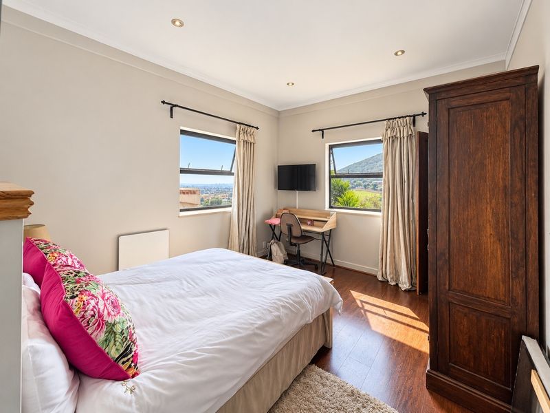 A well-lit bedroom featuring laminate flooring, recessed downlights, and dual windows offering scenic views.