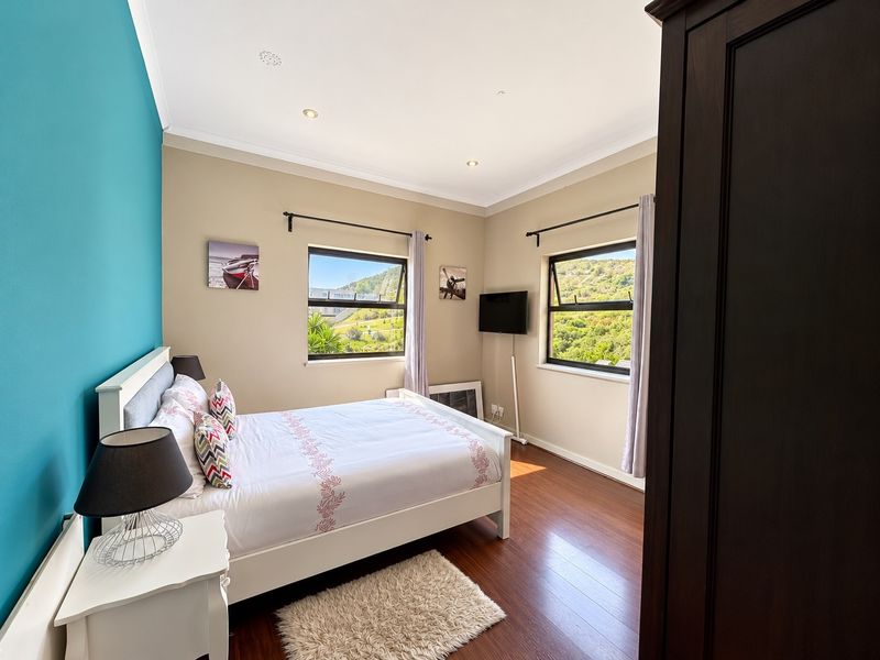 A well-maintained bedroom featuring laminate flooring, recessed downlighting, and dual windows offering scenic hillside views.