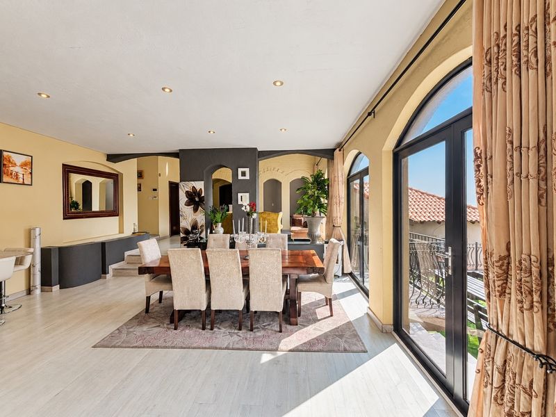 Spacious dining area featuring arched glass doors leading to a balcony, recessed lighting, and neutral finishes, creating a bright and inviting atmosphere.
