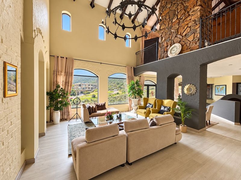 Spacious double-volume living room featuring a striking stone fireplace, exposed timber beams, and large arched windows offering scenic views.