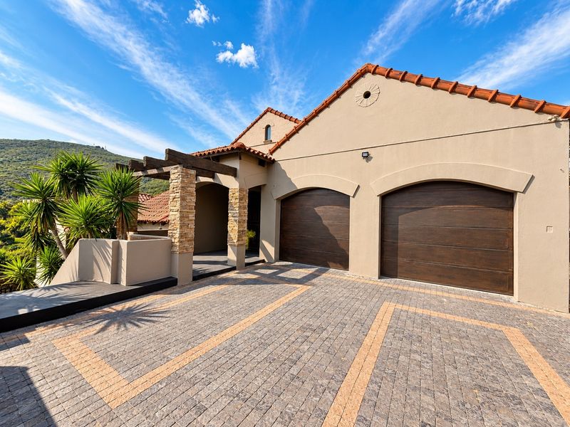 Front elevation featuring a double garage with timber doors, stone-clad pillars, a decorative pergola, and a well-maintained paved driveway.