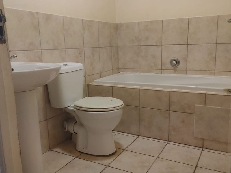 A functional bathroom featuring a pedestal basin, toilet, and bathtub with neutral wall and floor tiling.