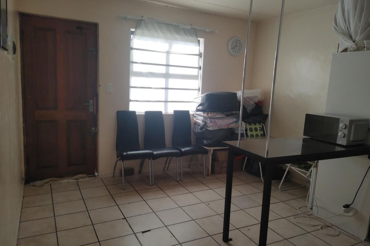 A living area featuring tiled flooring, a timber entrance door, and a window with security bars, requiring cosmetic updates to improve its overall condition.