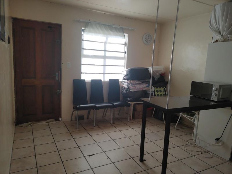 A living area featuring tiled flooring, a timber entrance door, and a window with security bars, requiring cosmetic updates to improve its overall condition.