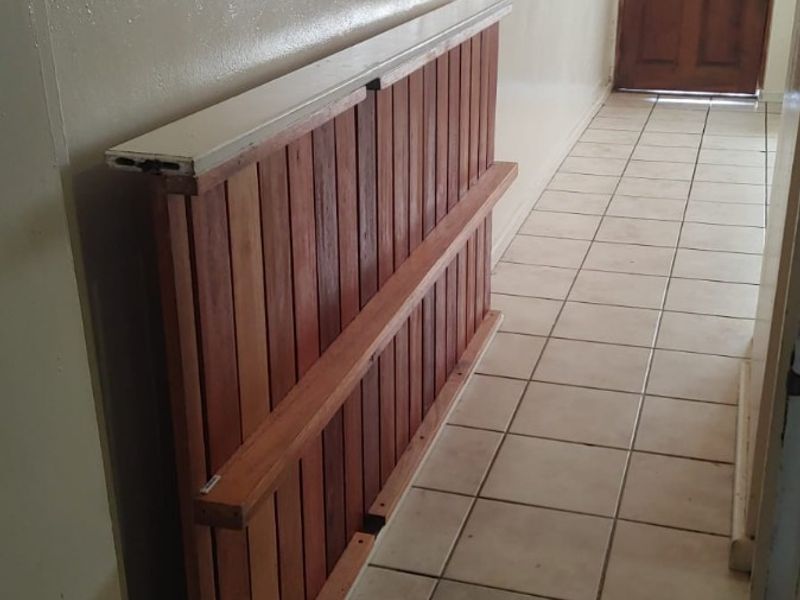A narrow hallway featuring tiled flooring and a wooden entrance door, currently used for storage of a timber partition.