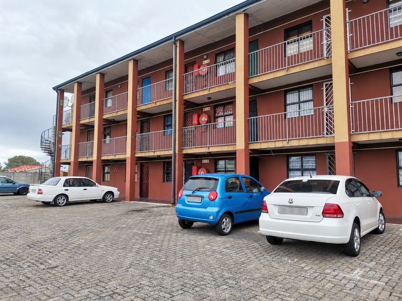 Exterior view of a multi-story apartment complex featuring paved parking, balconies with metal railings, and external fire safety equipment.