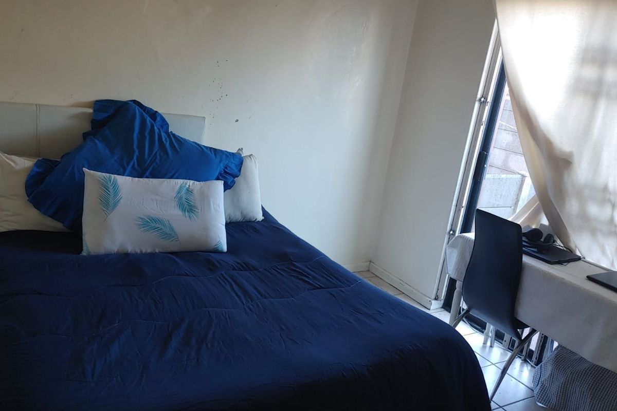 A bedroom featuring tiled flooring and a sliding glass door providing natural light. The space requires minor wall repairs and cosmetic updates.