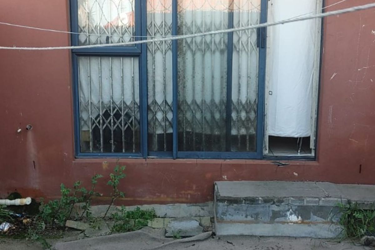 Rear exterior view of the apartment featuring a sliding glass door with security gate, concrete patio area, and weathered exterior wall finish.