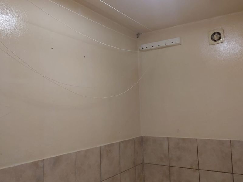 A functional laundry area featuring a retractable clothesline, wall-mounted extractor fan, and partial wall tiling.