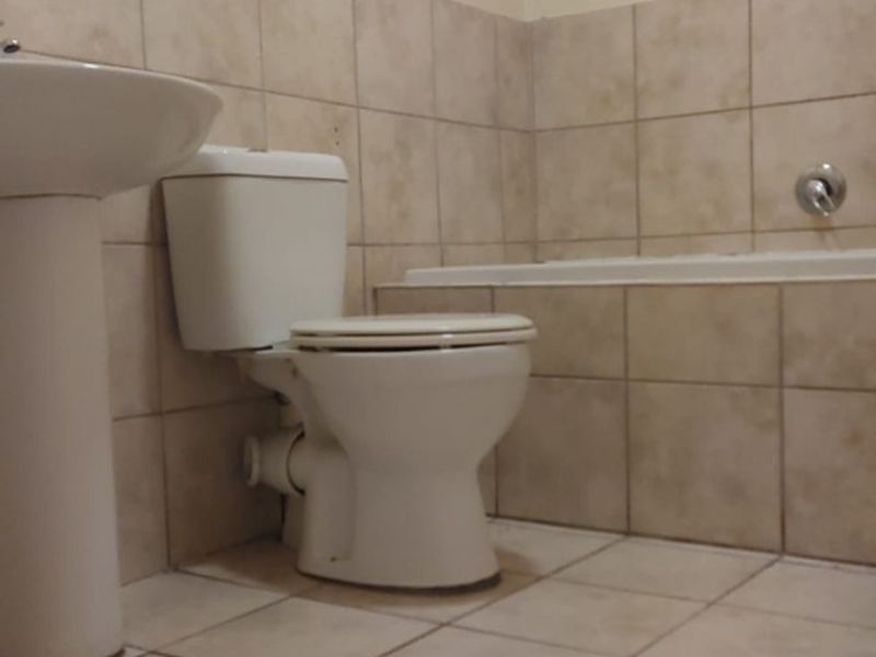 A functional bathroom featuring a pedestal basin, toilet, and bathtub with neutral ceramic wall and floor tiling.