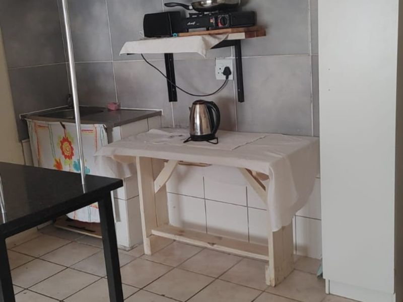 A compact kitchen area featuring white built-in cabinetry, grey tiled splashbacks, and tiled flooring, requiring some maintenance and modernization.
