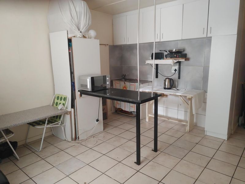 A compact kitchen area featuring white cabinetry, tiled splashbacks, and a breakfast bar, currently requiring significant renovation and modernization of fixed finishes.