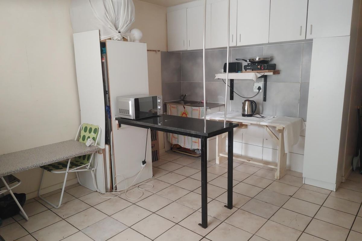 A compact kitchen area featuring white cabinetry, tiled splashbacks, and a breakfast bar, currently requiring significant renovation and modernization of fixed finishes.
