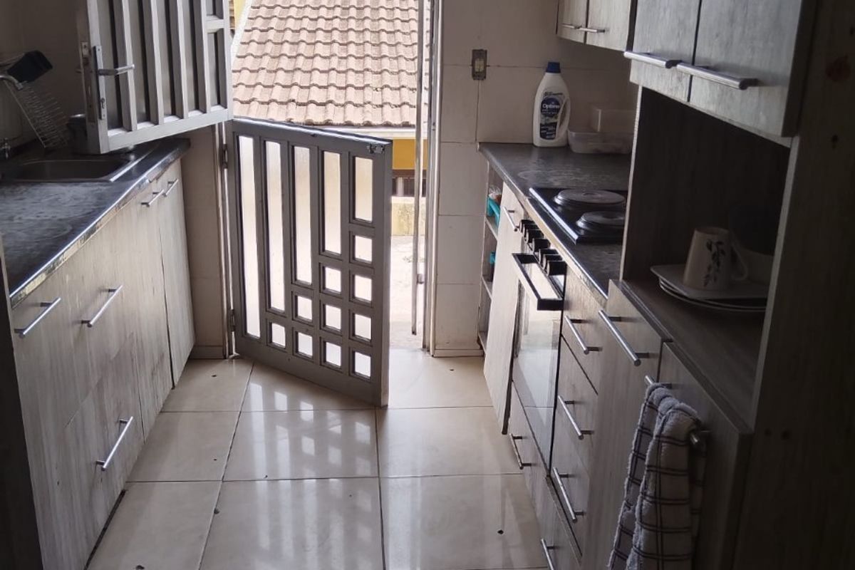 A functional galley-style kitchen featuring wood-look cabinetry, built-in oven, cooktop, and direct access to an outdoor area through a security gate.