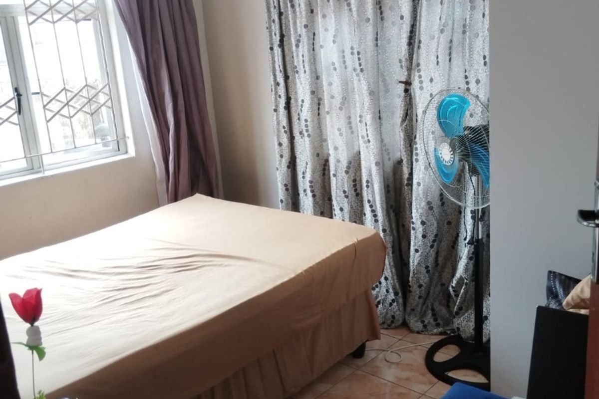 A functional bedroom featuring tiled flooring and a window fitted with security bars, providing a practical and secure living space.