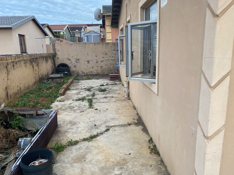 A rear exterior view of the property featuring a concrete patio area, boundary wall, and casement windows, currently requiring maintenance and landscaping.