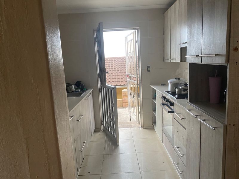 A functional galley-style kitchen featuring built-in cabinetry, a hob, an oven, and tiled flooring, with direct access to an outdoor area via a security gate.