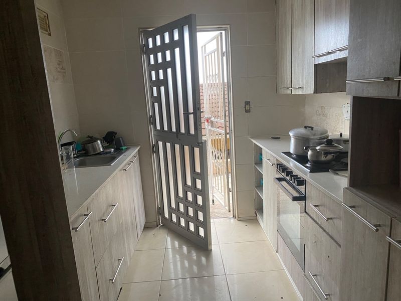 A functional galley-style kitchen featuring wood-look cabinetry, stone countertops, built-in oven and hob, and direct access to an outdoor area via a security gate.
