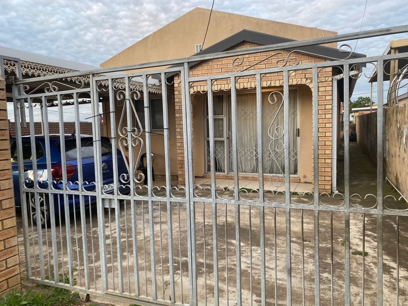 Front view of a single-story brick house featuring a metal security gate, concrete driveway, and a sliding glass door with security bars.