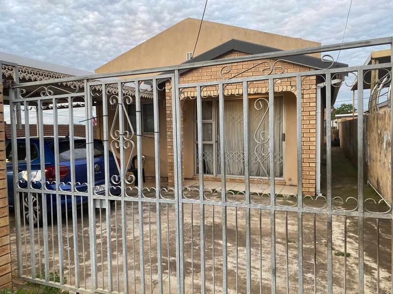 Front elevation of a single-story brick house featuring a metal security gate, concrete driveway, and a covered patio entrance.