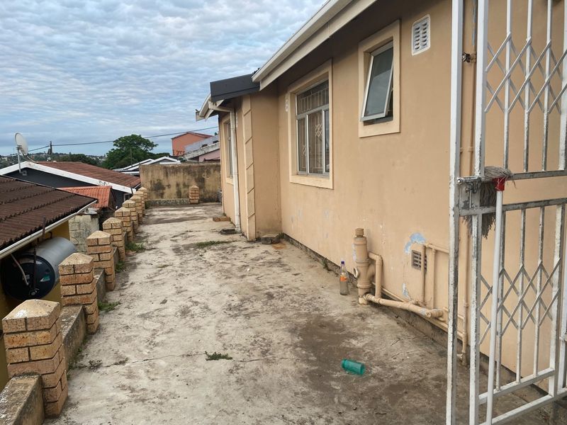 Rear exterior patio area featuring concrete flooring, brick boundary walling, and security gate access, showing signs of weathering and wear.