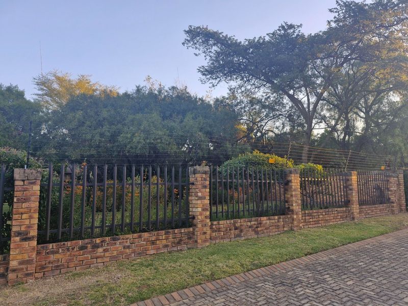 A secure street-facing boundary featuring a brick and steel palisade fence topped with electric security wiring.