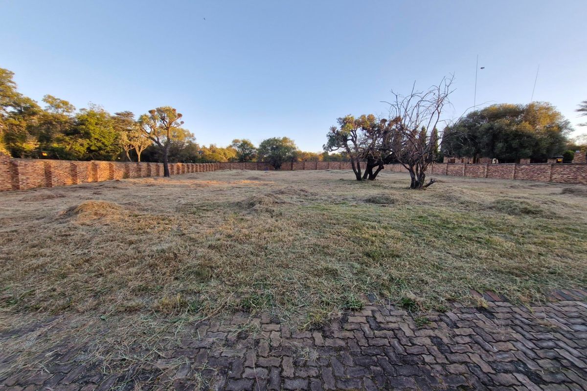 A spacious, level residential plot featuring a brick perimeter wall and established trees, offering a blank canvas for future development.