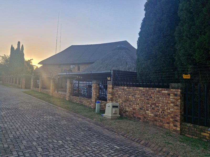 Front exterior view of a residential property featuring a brick boundary wall, electric fencing, and a traditional thatch roof structure.