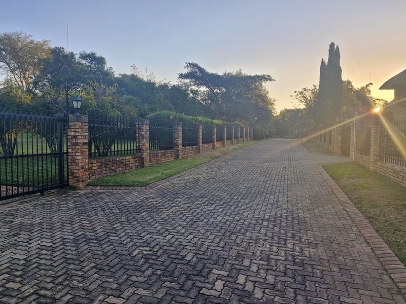 A well-maintained brick paved driveway leading to the property entrance, featuring secure brick boundary walls with metal and electric fencing.