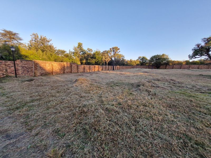 A vacant residential plot featuring a perimeter brick wall and established trees, offering a clear space for future development.
