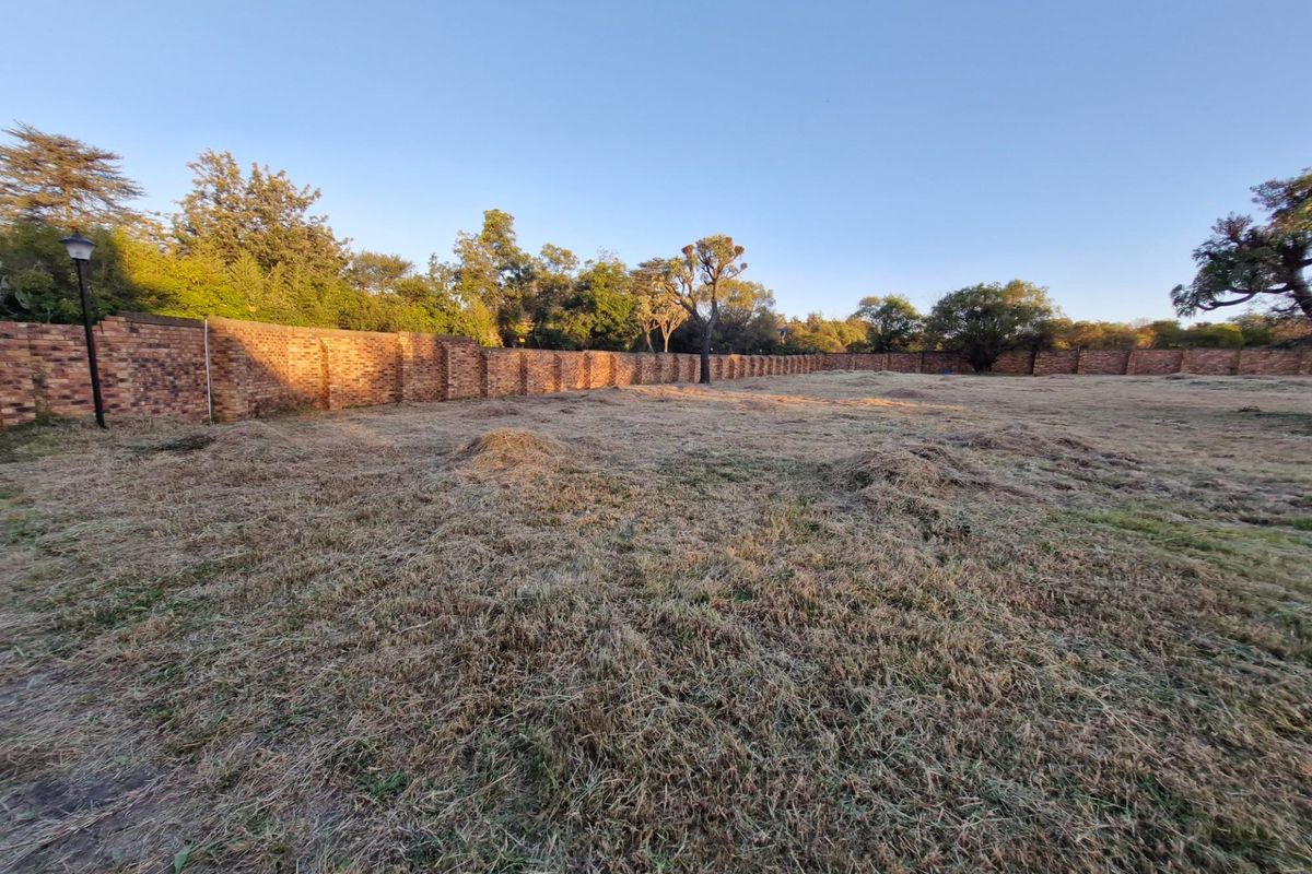A vacant residential plot featuring a perimeter brick wall and established trees, offering a clear space for future development.