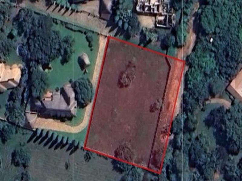 Aerial view of a vacant residential plot outlined in red, situated within a established neighborhood with surrounding mature trees and neighboring properties.
