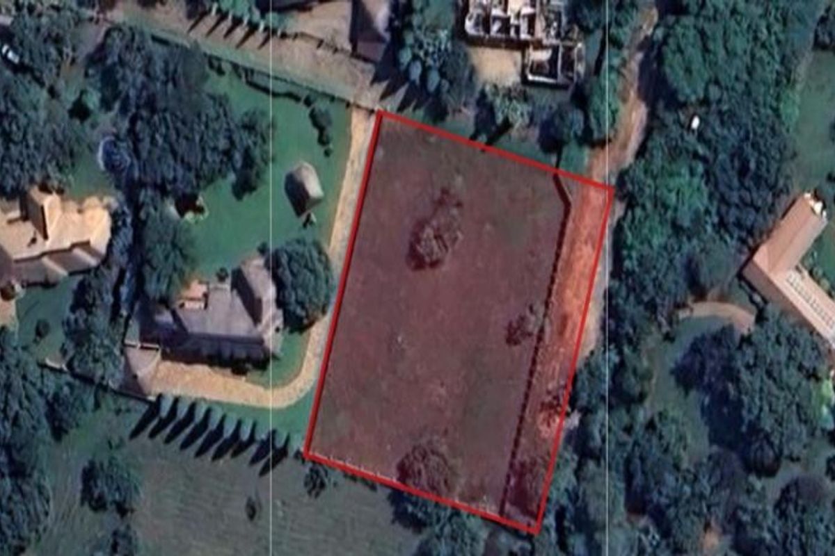 Aerial view of a vacant residential plot outlined in red, situated within a established neighborhood with surrounding mature trees and neighboring properties.