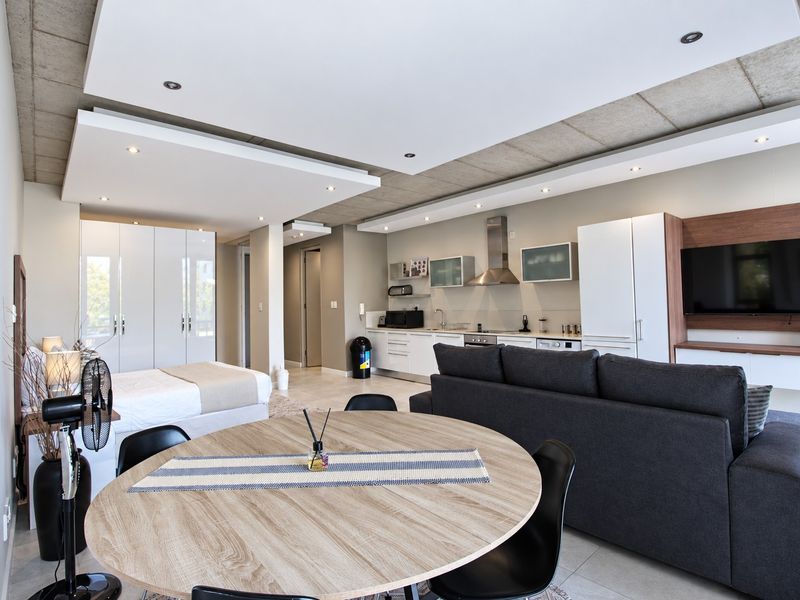 Modern open-plan apartment featuring a sleek kitchen with built-in appliances, recessed ceiling lighting, and integrated storage solutions in a contemporary living space.