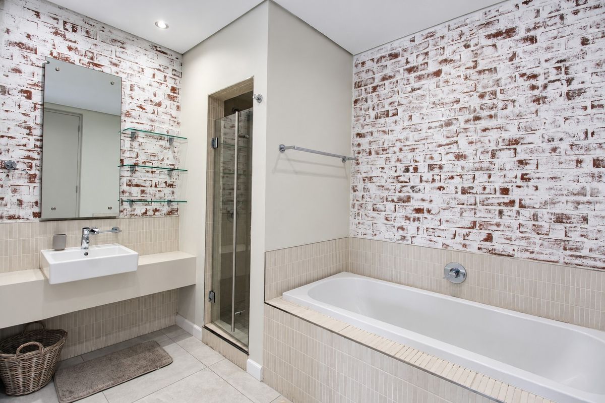 Modern bathroom featuring an exposed brick wall, built-in bathtub, separate glass shower enclosure, and a wall-mounted basin with glass shelving.