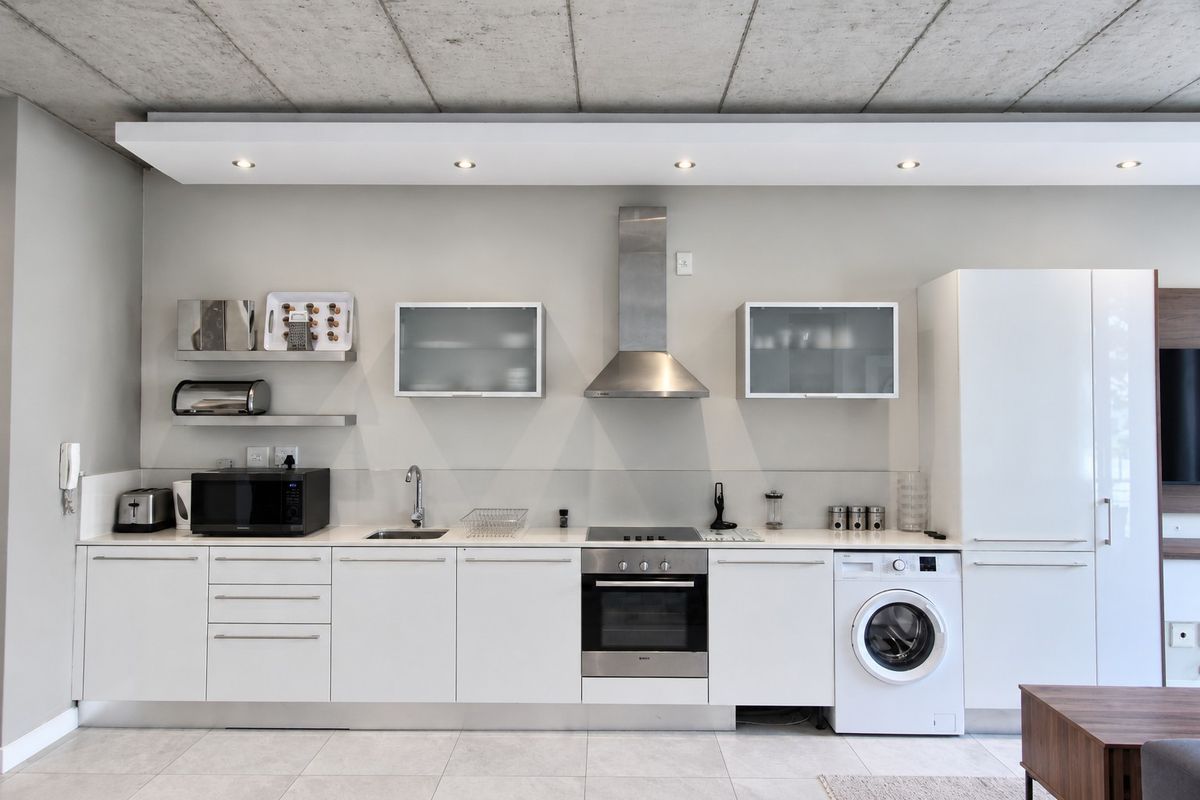 Modern kitchen featuring white cabinetry, stainless steel appliances, integrated washing machine, and a contemporary exposed concrete ceiling with recessed lighting.