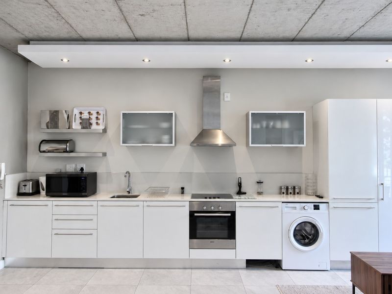 Modern kitchen featuring white cabinetry, stainless steel appliances, integrated washing machine, and a contemporary exposed concrete ceiling with recessed lighting.