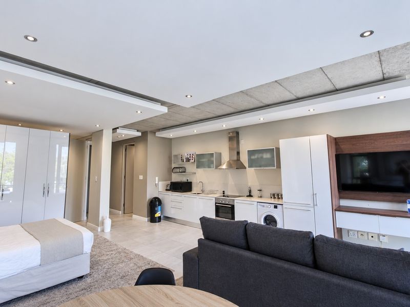 Modern open-plan studio apartment featuring a sleek kitchen with integrated appliances, built-in cabinetry, and a contemporary exposed concrete ceiling design.