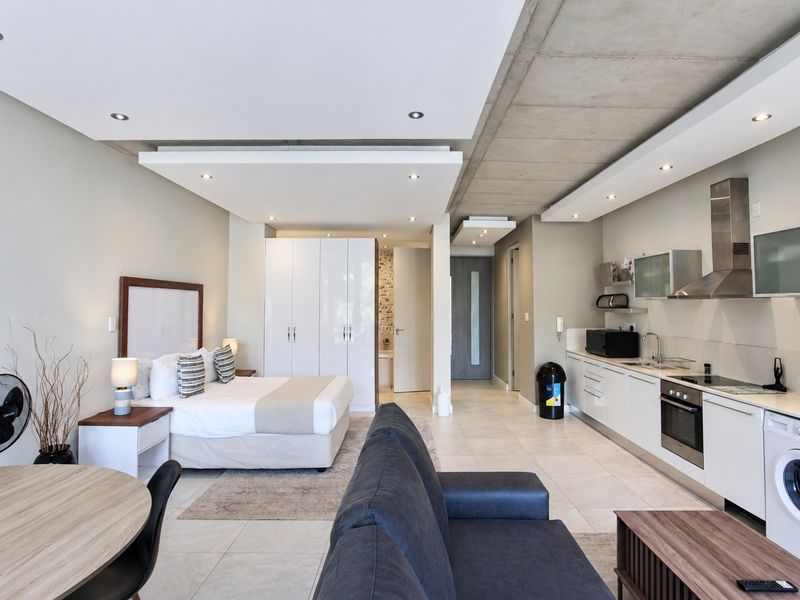 Modern open-plan studio apartment featuring a sleek kitchen with integrated appliances, exposed concrete ceiling, and built-in storage, finished with contemporary tiled flooring.