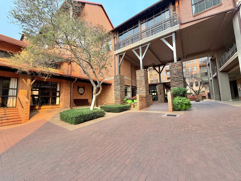 A well-maintained brick residential building exterior featuring stone-clad pillars, a paved courtyard area, and a covered walkway with balcony access.