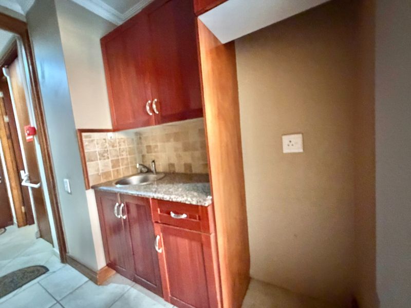 A compact scullery area featuring wooden cabinetry, granite countertops, a stainless steel sink, and tiled backsplash, providing functional prep space.