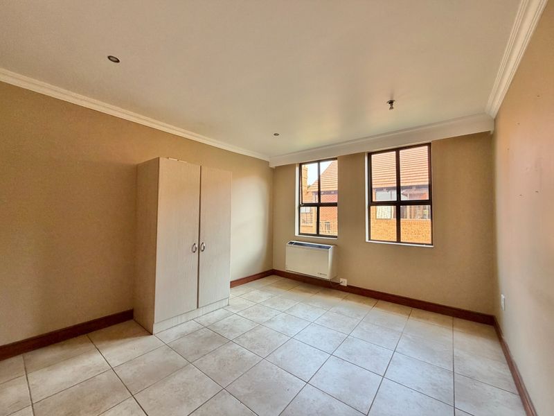 A bright, empty bedroom featuring tiled flooring, a built-in wardrobe, and a wall-mounted air conditioning unit.