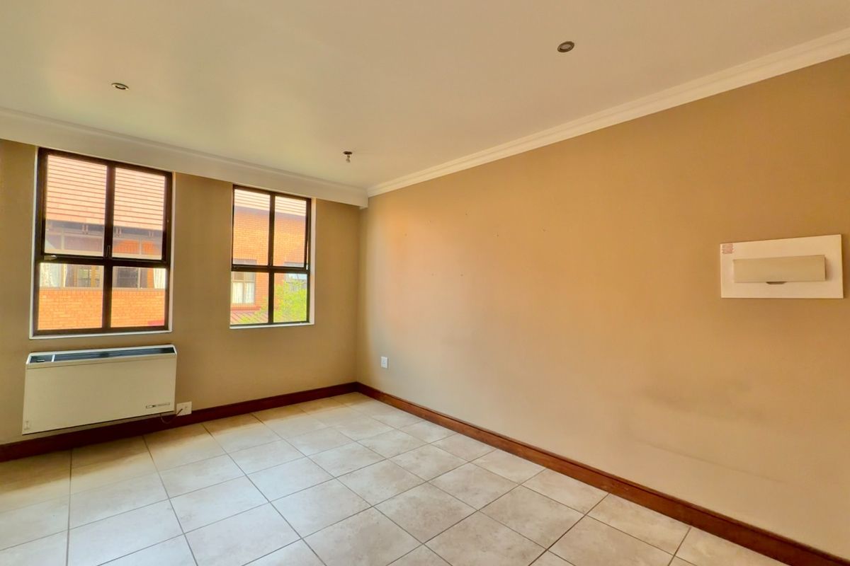 An empty bedroom featuring tiled flooring, recessed lighting, and a built-in air conditioning unit, offering a neutral canvas for personalization.