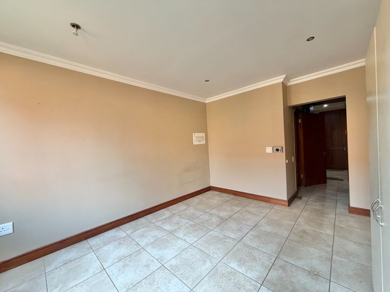 An empty bedroom featuring neutral wall paint, tiled flooring, recessed lighting, and a built-in cupboard, providing a blank canvas for personalization.