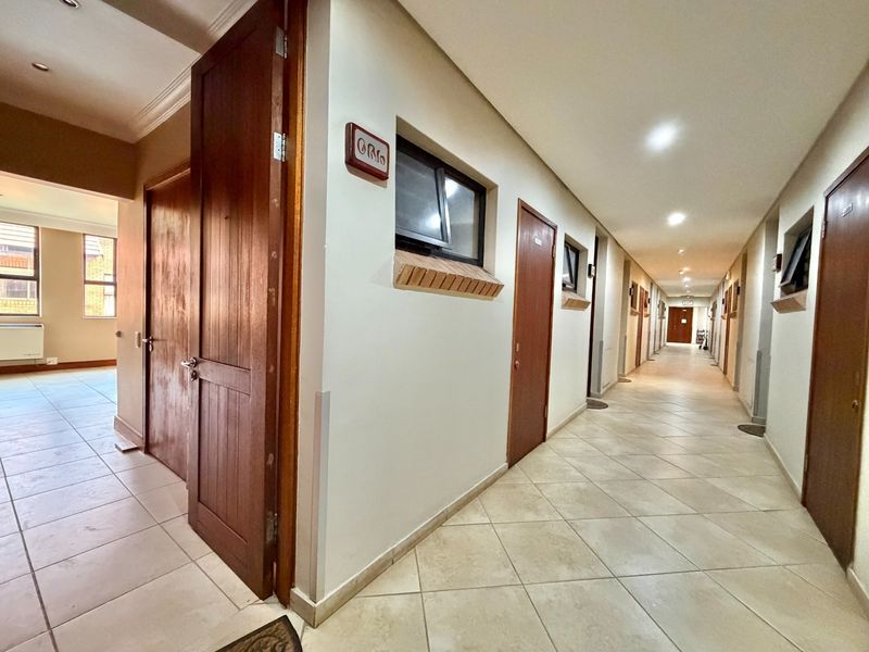 A long, well-lit interior hallway featuring tiled flooring, multiple timber doors, and small awning windows along the wall.